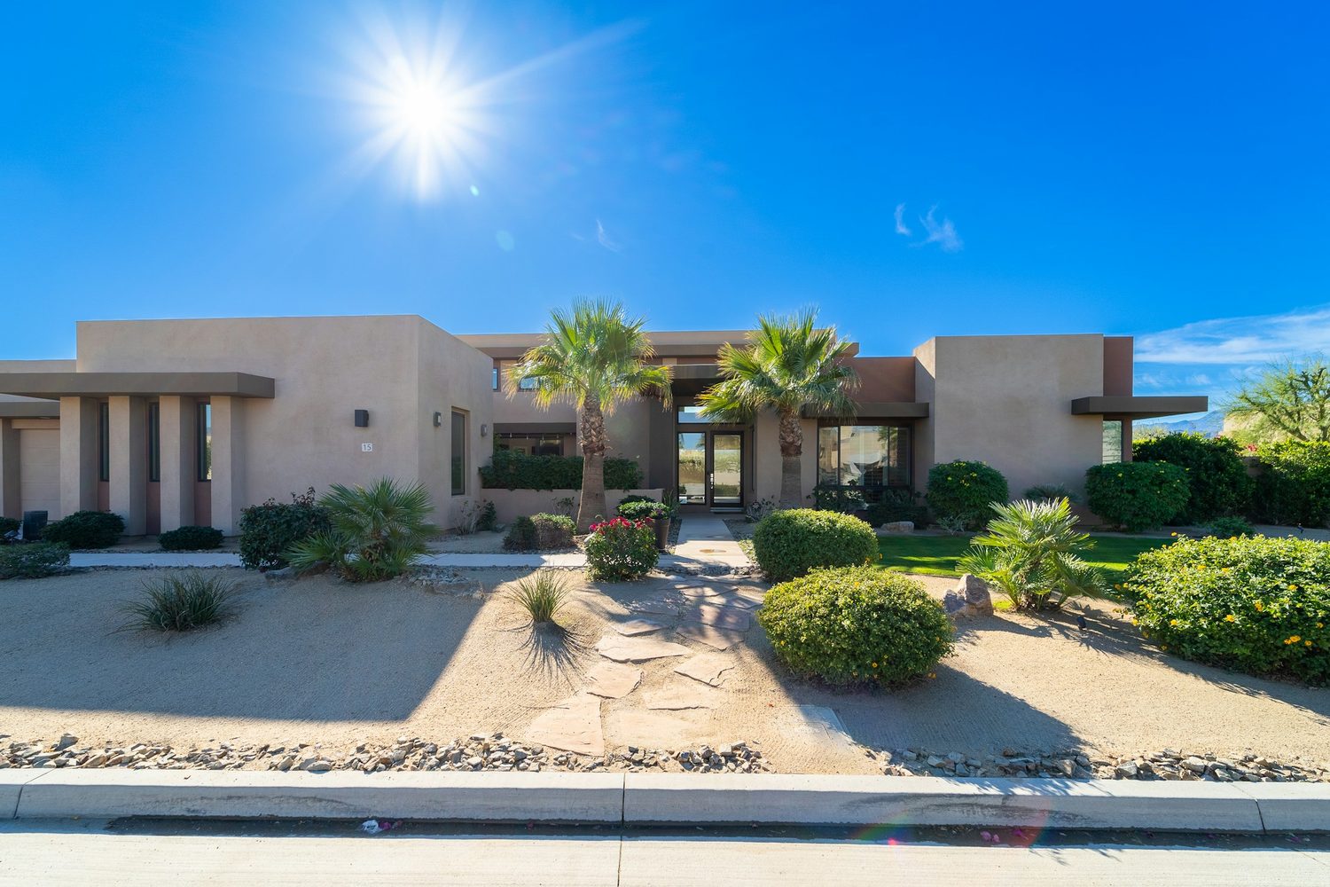 A single-storey Southwest home in daylight, palms and desert planting out front